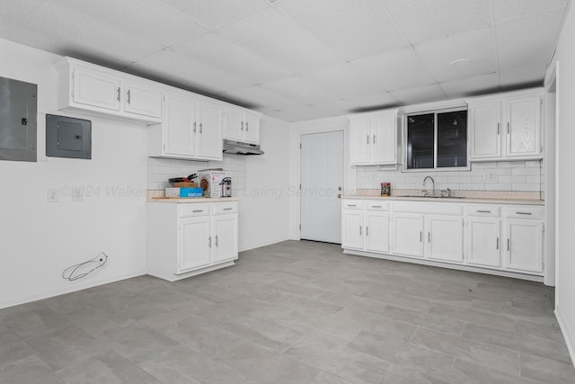 kitchen with decorative backsplash, electric panel, white cabinetry, and sink