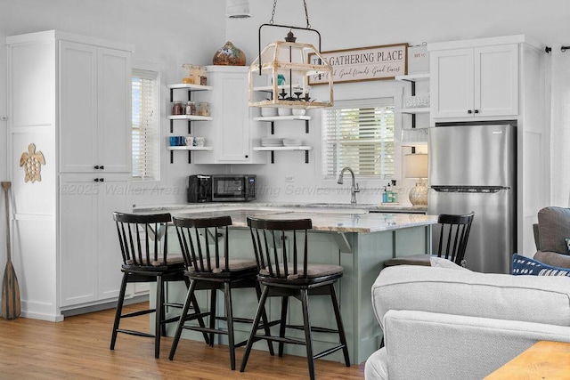 kitchen featuring light stone countertops, white cabinets, sink, stainless steel refrigerator, and a breakfast bar area