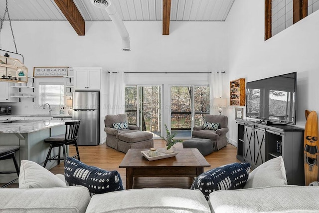 living room with a healthy amount of sunlight, light hardwood / wood-style flooring, and beamed ceiling