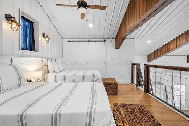 bedroom featuring ceiling fan, a barn door, and hardwood / wood-style flooring