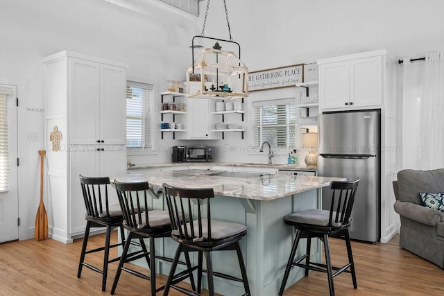 kitchen featuring a center island, sink, stainless steel refrigerator, light stone countertops, and white cabinets