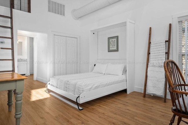 bedroom with wood-type flooring, a towering ceiling, and a closet