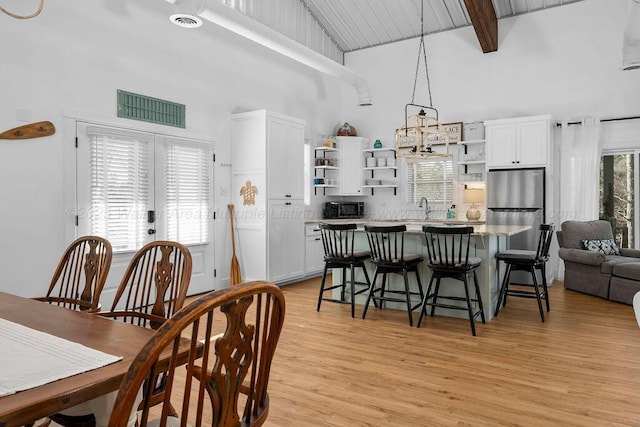 dining space featuring sink, beamed ceiling, a high ceiling, and light hardwood / wood-style flooring