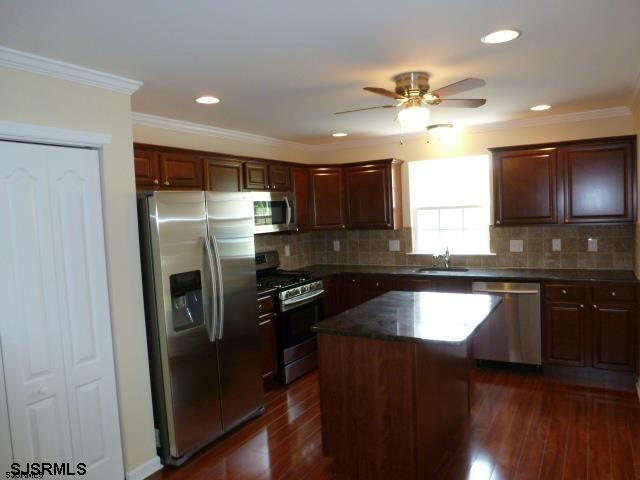 kitchen featuring dark wood-type flooring, appliances with stainless steel finishes, a kitchen island, ceiling fan, and sink