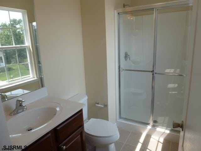 bathroom featuring tile floors, toilet, vanity, and a shower with door