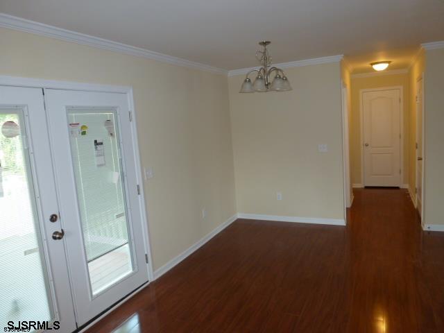 empty room featuring an inviting chandelier, dark hardwood / wood-style floors, french doors, and ornamental molding