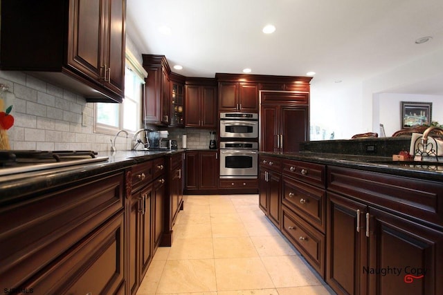 kitchen with dark stone counters, appliances with stainless steel finishes, backsplash, sink, and light tile flooring