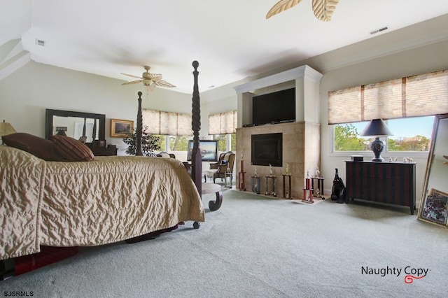 carpeted bedroom with ceiling fan and a tiled fireplace