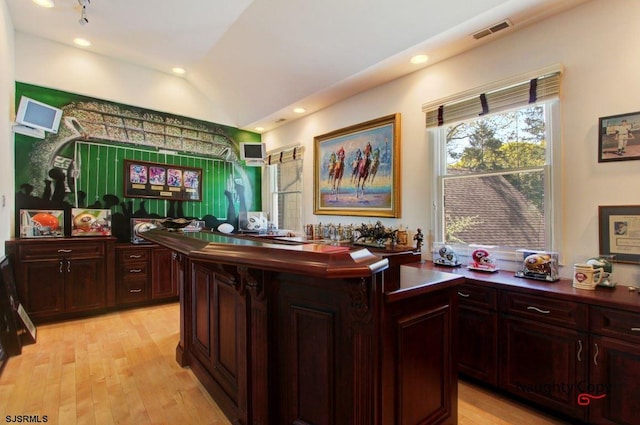 bar featuring lofted ceiling, dark brown cabinetry, and light hardwood / wood-style flooring