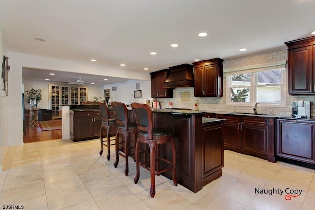 kitchen featuring a kitchen bar, custom range hood, ceiling fan, sink, and light tile flooring