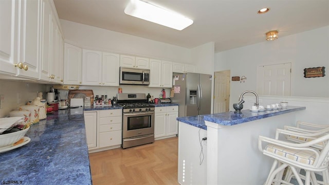 kitchen featuring light parquet flooring, appliances with stainless steel finishes, white cabinetry, dark stone countertops, and sink