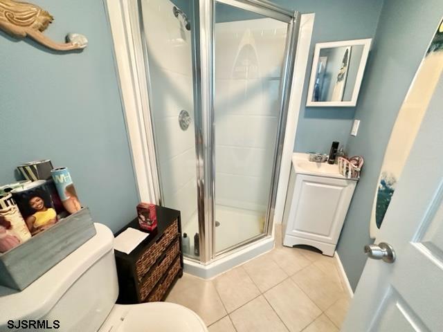 bathroom featuring a shower with shower door, toilet, vanity, and tile patterned floors