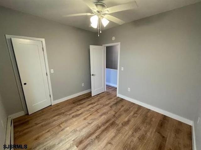 unfurnished bedroom featuring a closet, baseboard heating, light hardwood / wood-style flooring, and ceiling fan