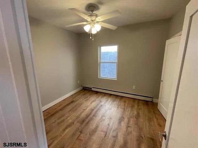 empty room with a baseboard heating unit, light wood-type flooring, and ceiling fan