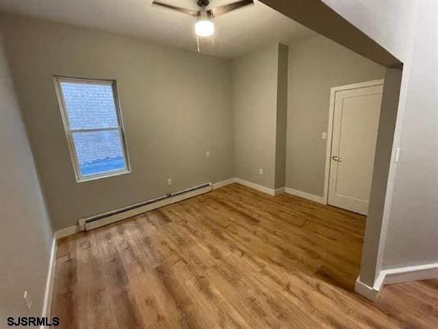 spare room with wood-type flooring, ceiling fan, and a baseboard radiator