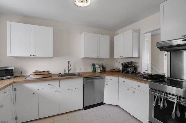 kitchen with appliances with stainless steel finishes, white cabinetry, light tile floors, butcher block counters, and sink