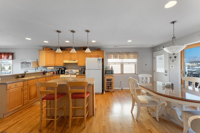 kitchen with light hardwood / wood-style floors, a kitchen island, pendant lighting, white appliances, and sink