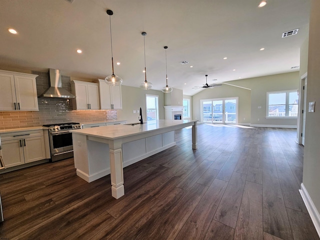 kitchen with white cabinetry, ceiling fan, wall chimney range hood, vaulted ceiling, and stainless steel range with gas stovetop