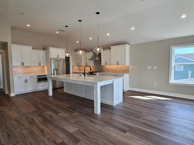 kitchen featuring high quality fridge, white cabinetry, wall chimney exhaust hood, and hanging light fixtures