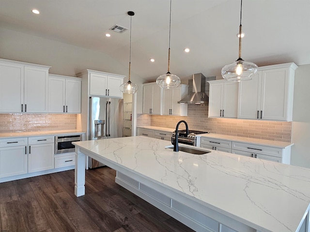 kitchen featuring wall chimney exhaust hood, sink, pendant lighting, a center island with sink, and white cabinetry