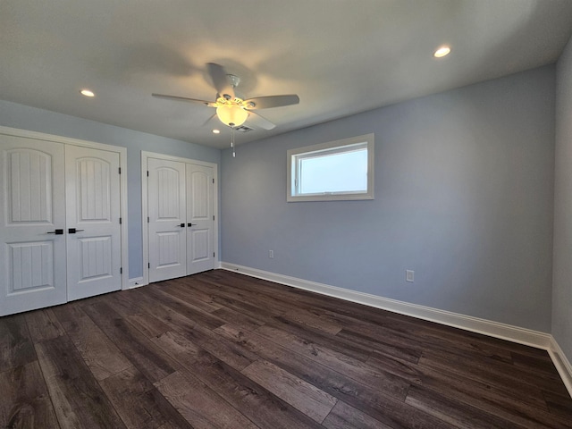 unfurnished bedroom with ceiling fan, dark hardwood / wood-style flooring, and multiple closets