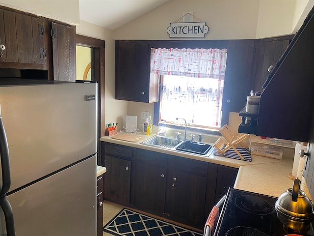 kitchen featuring range, dark brown cabinets, stainless steel fridge, lofted ceiling, and sink