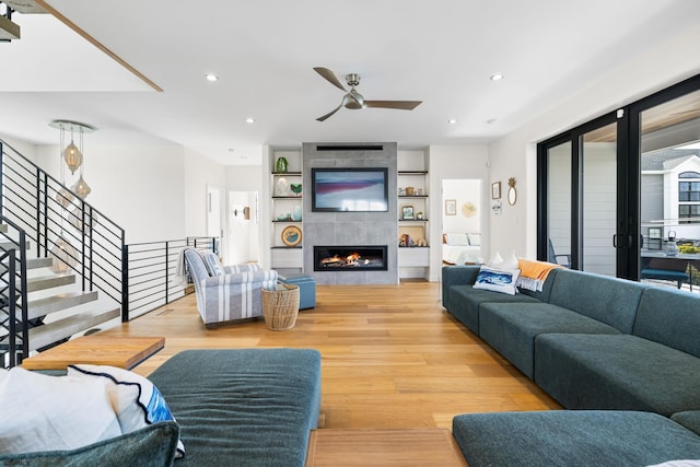 living room with built in features, light hardwood / wood-style floors, ceiling fan, and a fireplace