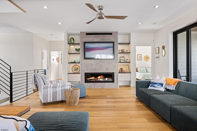 living room featuring light hardwood / wood-style flooring, ceiling fan, a fireplace, and built in shelves