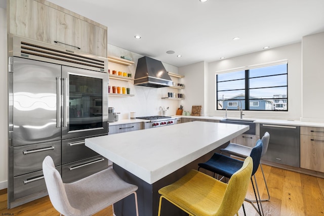 kitchen with a center island, light hardwood / wood-style floors, wall chimney range hood, a breakfast bar area, and stainless steel appliances