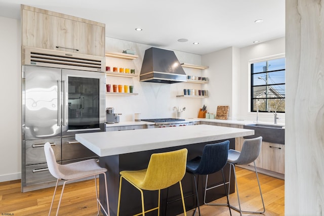 kitchen featuring wall chimney exhaust hood, light brown cabinetry, and light wood-type flooring