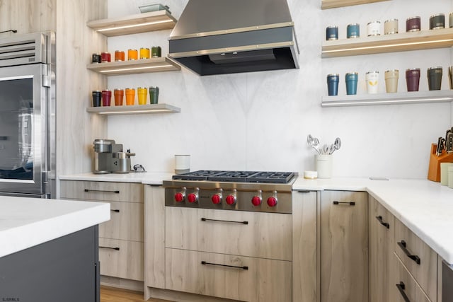 kitchen with light brown cabinets, hardwood / wood-style flooring, oven, stainless steel gas cooktop, and wall chimney exhaust hood