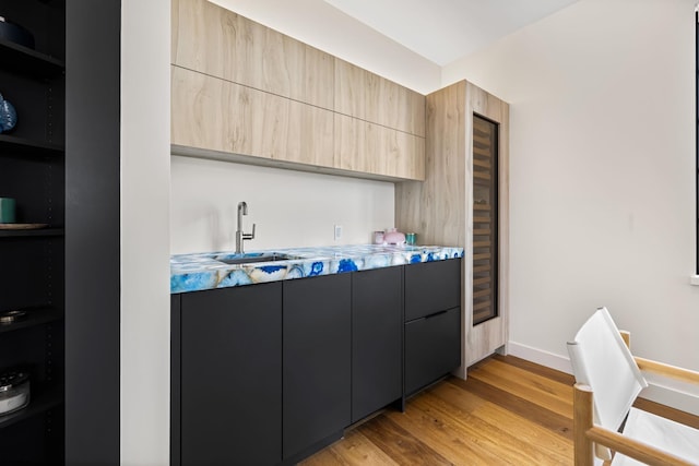 kitchen featuring light brown cabinetry, sink, light hardwood / wood-style flooring, and light stone countertops