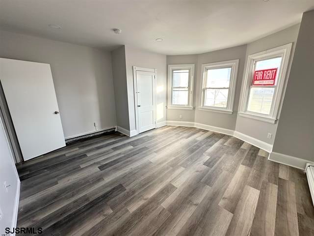 unfurnished room with baseboard heating, dark wood-type flooring, and a healthy amount of sunlight