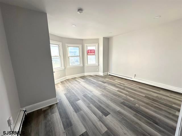 empty room with a baseboard radiator and dark hardwood / wood-style floors