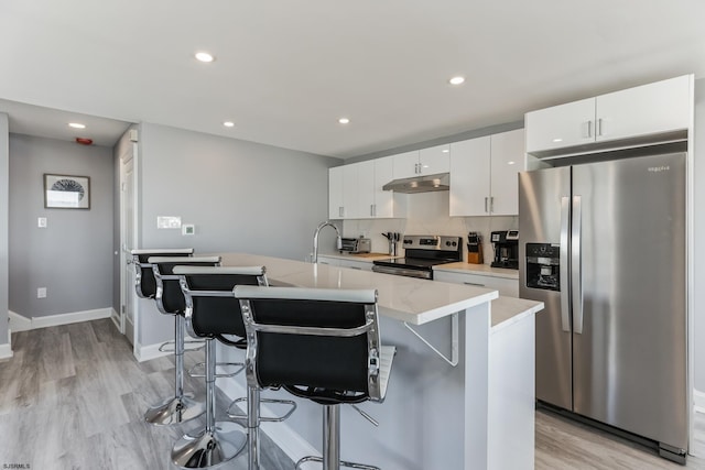 kitchen with light wood-type flooring, a breakfast bar, stainless steel appliances, a center island with sink, and white cabinets