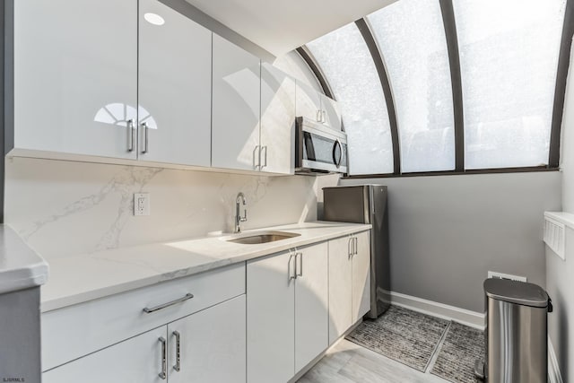 kitchen with sink, white cabinetry, light stone counters, and tasteful backsplash