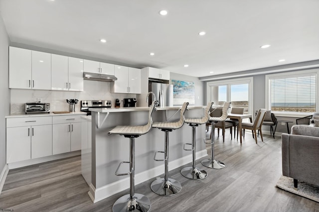 kitchen featuring a breakfast bar area, light hardwood / wood-style flooring, stainless steel appliances, and white cabinetry