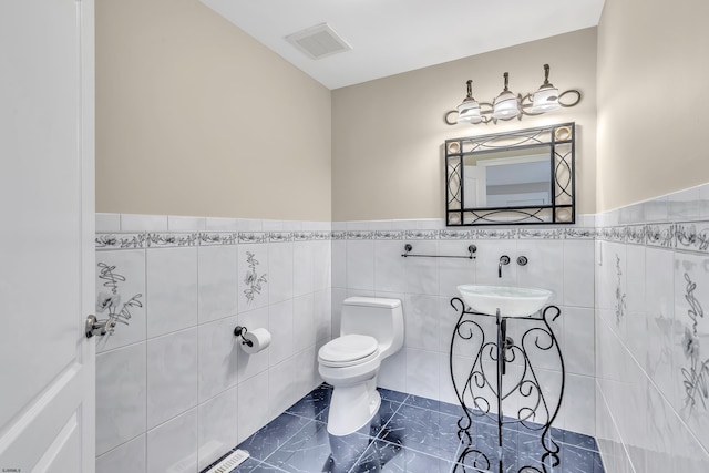 bathroom with toilet, tile flooring, tile walls, and sink