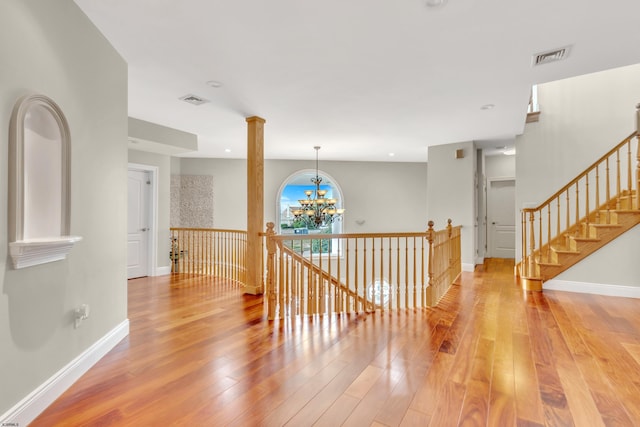 interior space with decorative columns, a notable chandelier, and light wood-type flooring