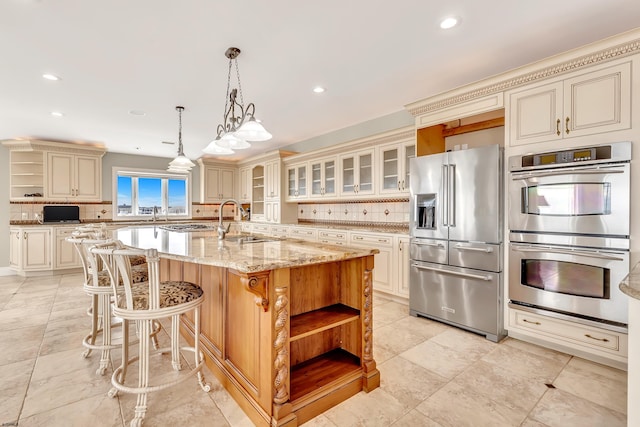 kitchen with light stone countertops, appliances with stainless steel finishes, backsplash, a kitchen island with sink, and pendant lighting