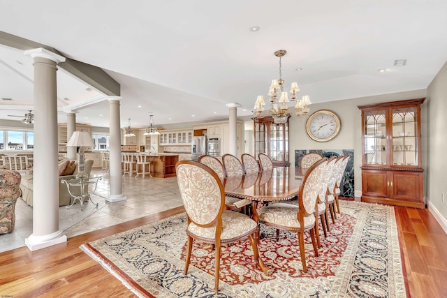 dining space with ceiling fan with notable chandelier, ornate columns, and light hardwood / wood-style floors