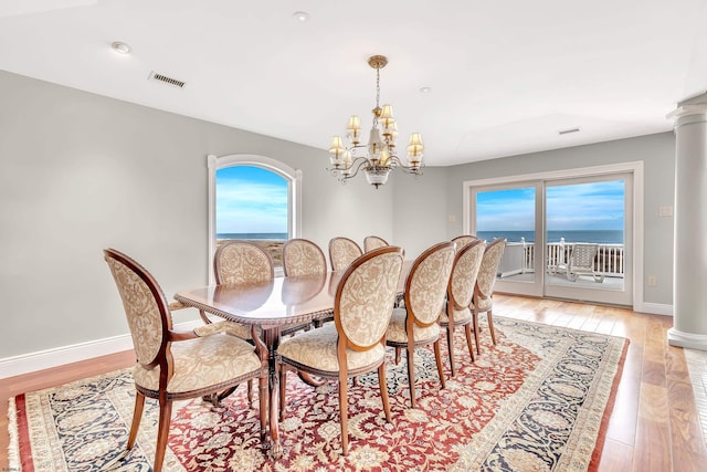 dining room with light wood-type flooring, decorative columns, a notable chandelier, and a water view