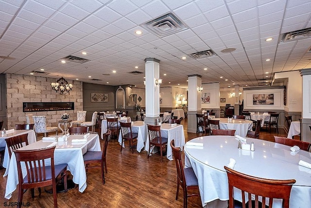 dining area featuring a large fireplace, dark wood-type flooring, a chandelier, and decorative columns