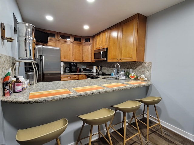 kitchen with appliances with stainless steel finishes, dark hardwood / wood-style floors, tasteful backsplash, and a kitchen bar