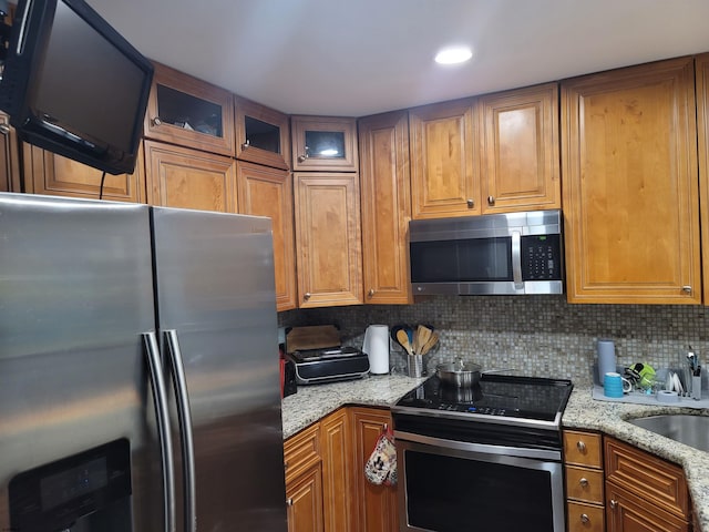 kitchen with tasteful backsplash, stainless steel appliances, sink, and light stone countertops