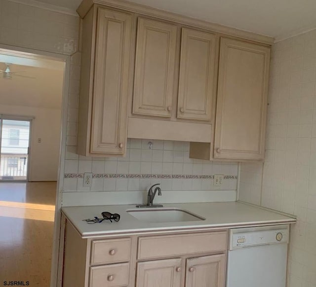 kitchen with sink, cream cabinetry, white dishwasher, and tile walls