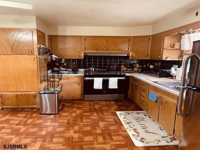 kitchen with appliances with stainless steel finishes, tasteful backsplash, wall chimney range hood, and light parquet floors