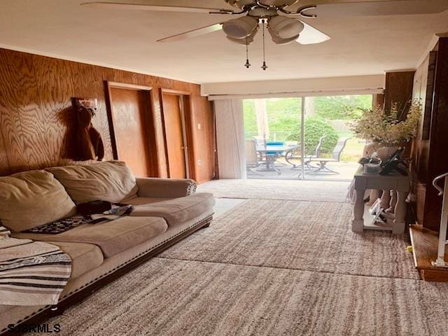 carpeted living room with wooden walls and ceiling fan