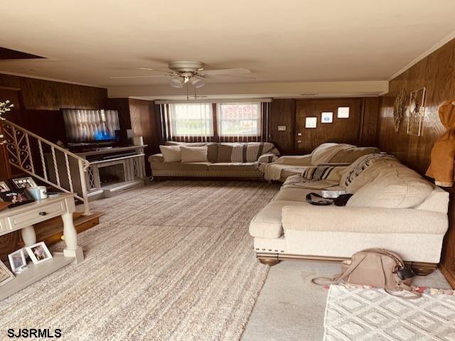 carpeted living room featuring ceiling fan and wood walls