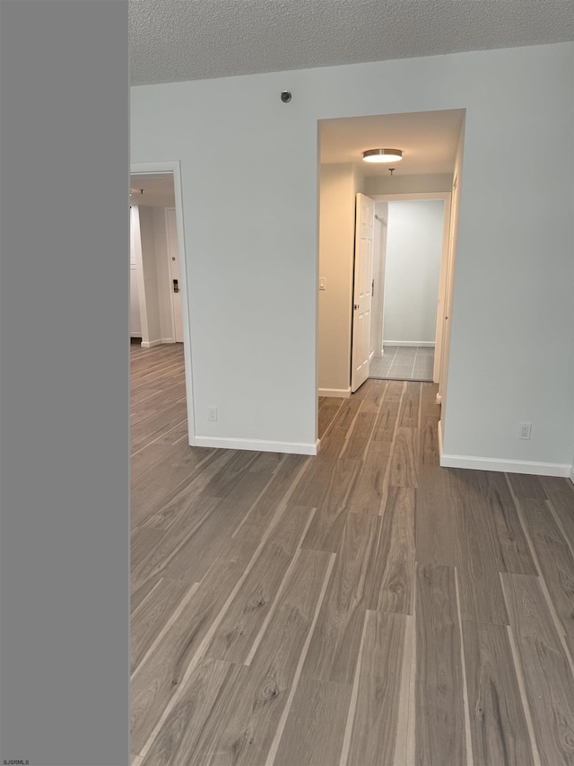 spare room with a textured ceiling, baseboards, and wood finished floors